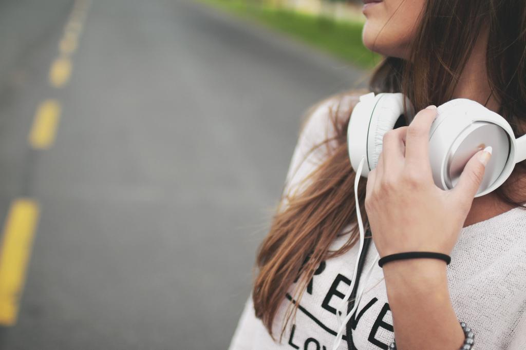 一个女孩站在混凝土路上的特写照片,拿着白色的无线耳机高清壁纸