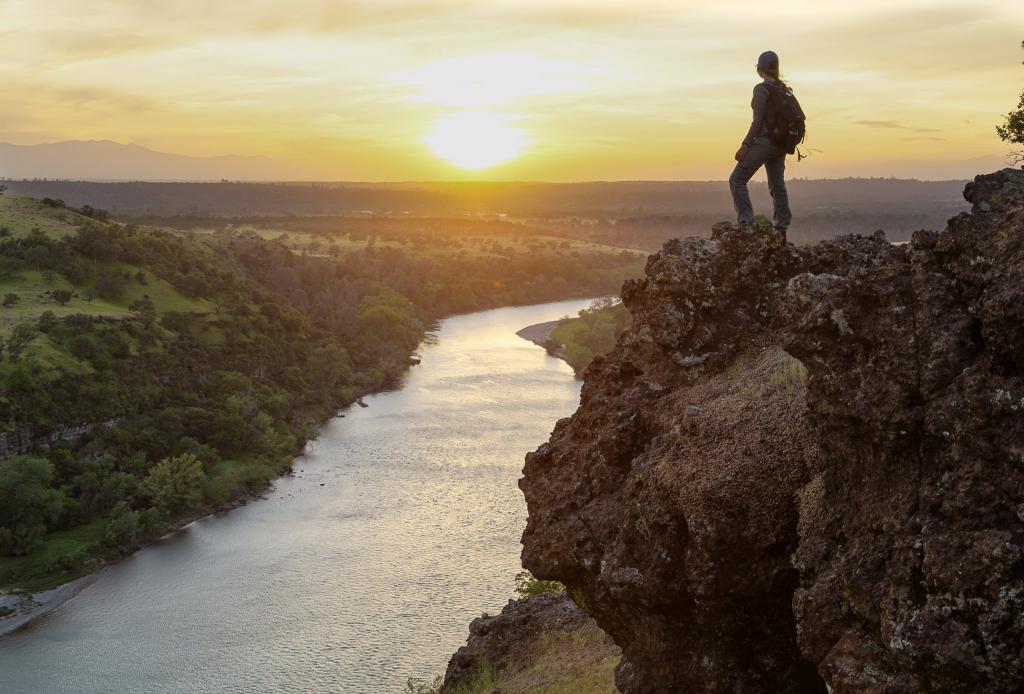 男子戴着背包站在岩石的悬崖上,面对日落面前河,萨克拉门托河高清壁纸