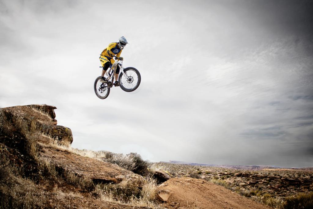 男子在黄色运动衫骑自行车在白天高清壁纸期间跳上棕色山悬崖