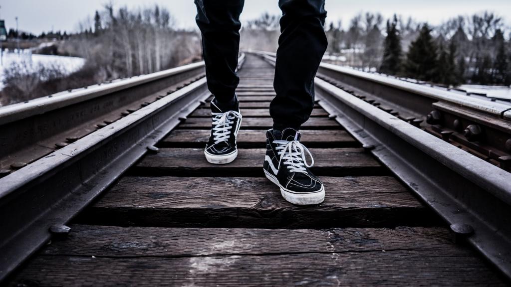 人穿黑色和白色的货车低顶运动鞋走在棕色铁路高清壁纸