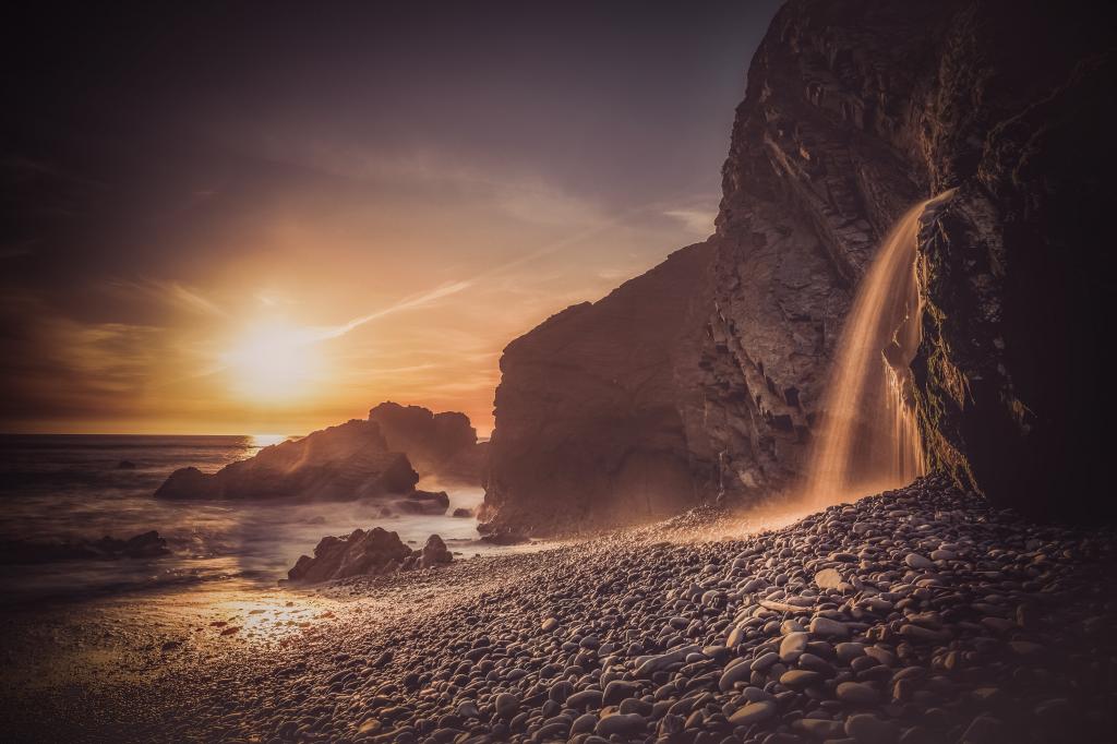 在日落期间的海边岩石山上的瀑布高清壁纸