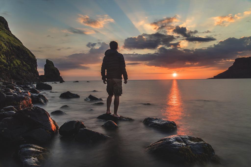 在日落期间高清壁纸站在海边石头上的连帽衫的男人