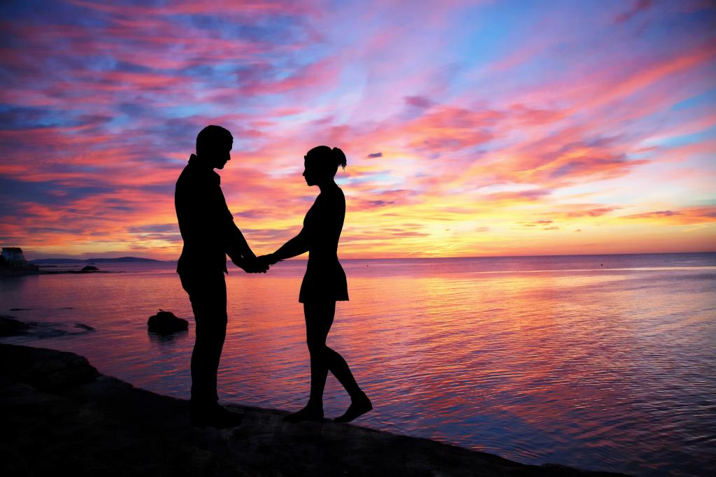 夫妇面对对方在日落期间高清壁纸海边