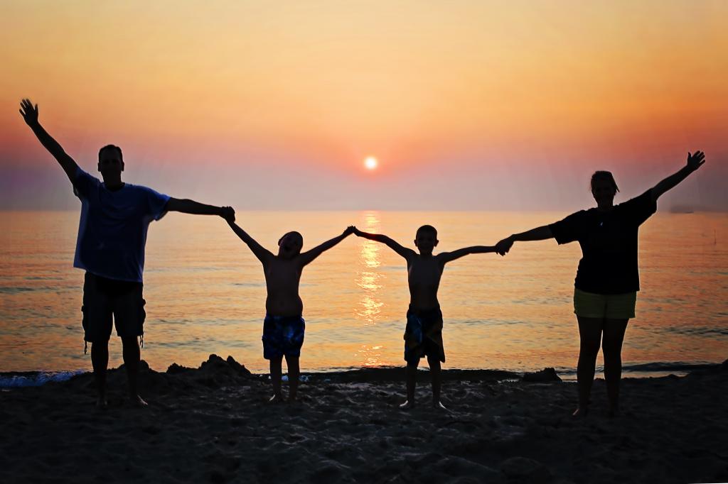 男人的剪影与他们的两个男孩举行的同时在日落期间举起双手在海滩的