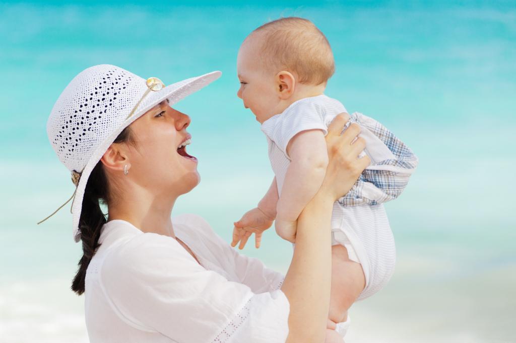 女人在白色的太阳帽子和衣服在白天高清壁纸附近的身体水域附近抱着一个婴儿