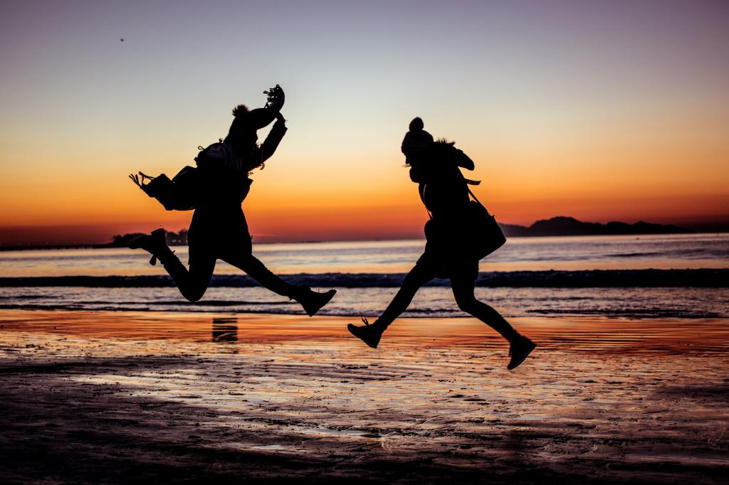 两个女人在日落期间跳海边剪影高清壁纸的剪影