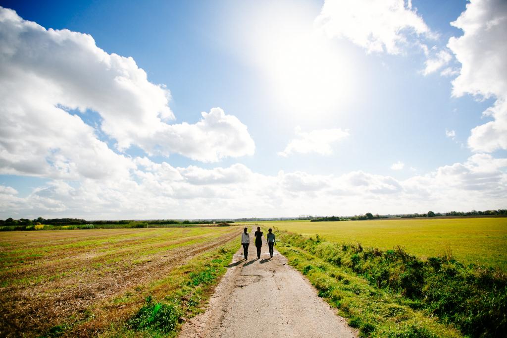 风景摄影的绿色的田野和泥土路与三人走在晴朗的天空下白天高清壁纸