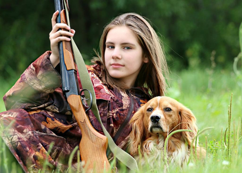 女孩旁边棕色的狗拿着步枪躺在白天高清壁纸树附近的草地上