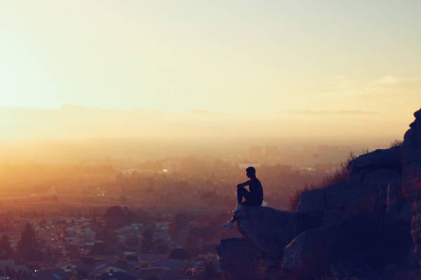 风景剪影摄影的人坐在悬崖上面对市区在金色的小时高清壁纸