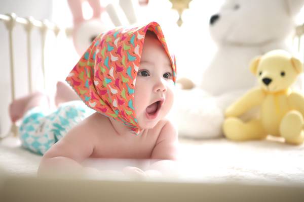 袒胸宝宝穿橙色,白色,绿色和红色的鸟类打印头巾旁边的白色和黄色的熊毛绒玩具高清壁纸
