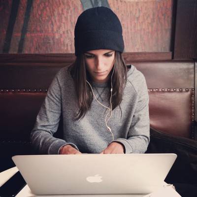 面对她的笔记本电脑穿着黑色针织帽和灰色外套与耳机高清壁纸的焦点照片