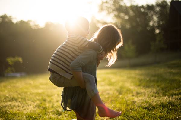 在阳光下高清壁纸下的绿色草地上的男孩在她身上的女孩