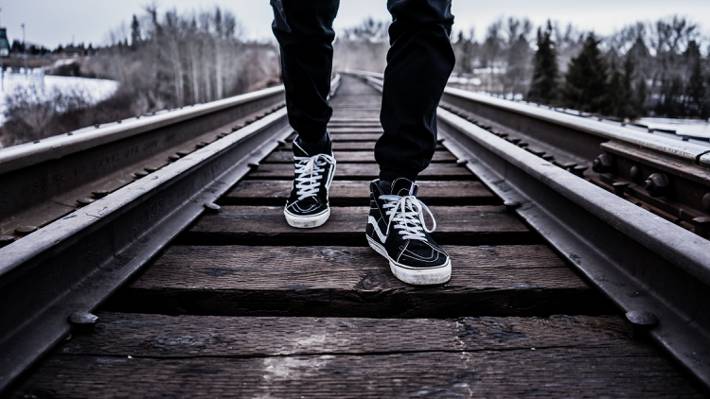 人穿黑色和白色的货车低顶运动鞋走在棕色铁路高清壁纸