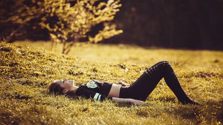 女人躺在草地上,她闭着眼睛,双腿弯曲高清壁纸