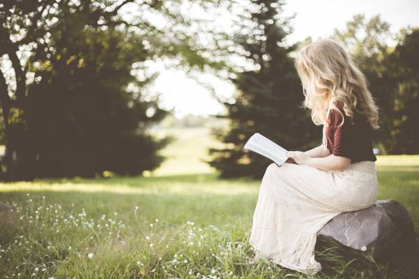 金色头发的女人坐在岩石上看书在白天高清壁纸