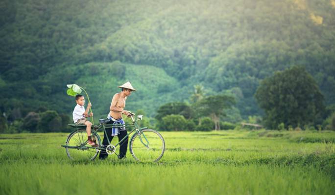 男人穿着黑色的裤子和圆顶的帽子推绿色的通勤自行车与男孩在附近山上的绿色草地上白天高清壁纸