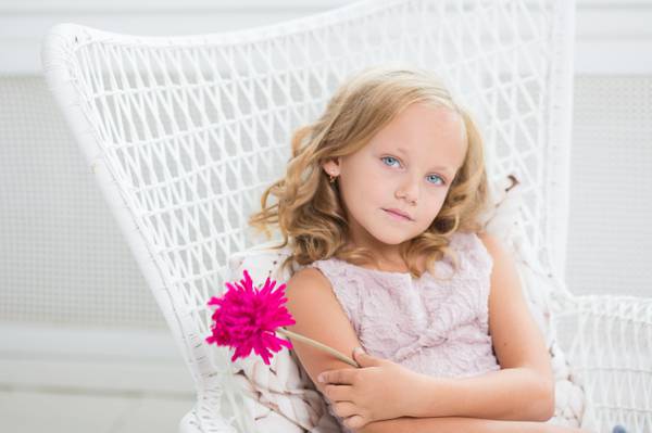 女孩抱着粉红色的花,坐在白色的扶手椅上高清壁纸
