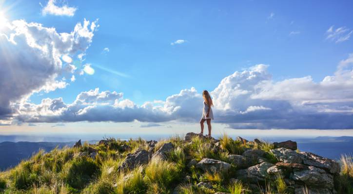 女人穿着白色的衣服站在悬崖上与岩石和草白天与多云的天空高清壁纸