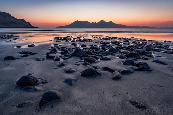 焦点的灰色石头在岸边的视图的远处山在日落时高清壁纸的照片