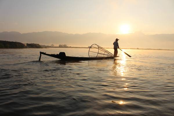 一艘渔夫在日落高清壁纸期间持有桨在水体的船上的剪影