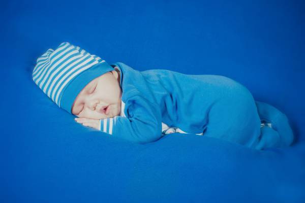 婴儿在蓝色的footie睡衣和白色和蓝色条纹针织帽睡在蓝色的垫高清壁纸