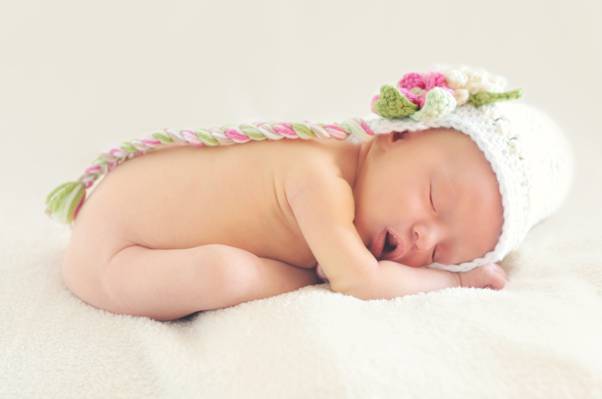 裸体婴儿在白色,绿色和粉红色的针织帽,躺在白色纺织高清壁纸