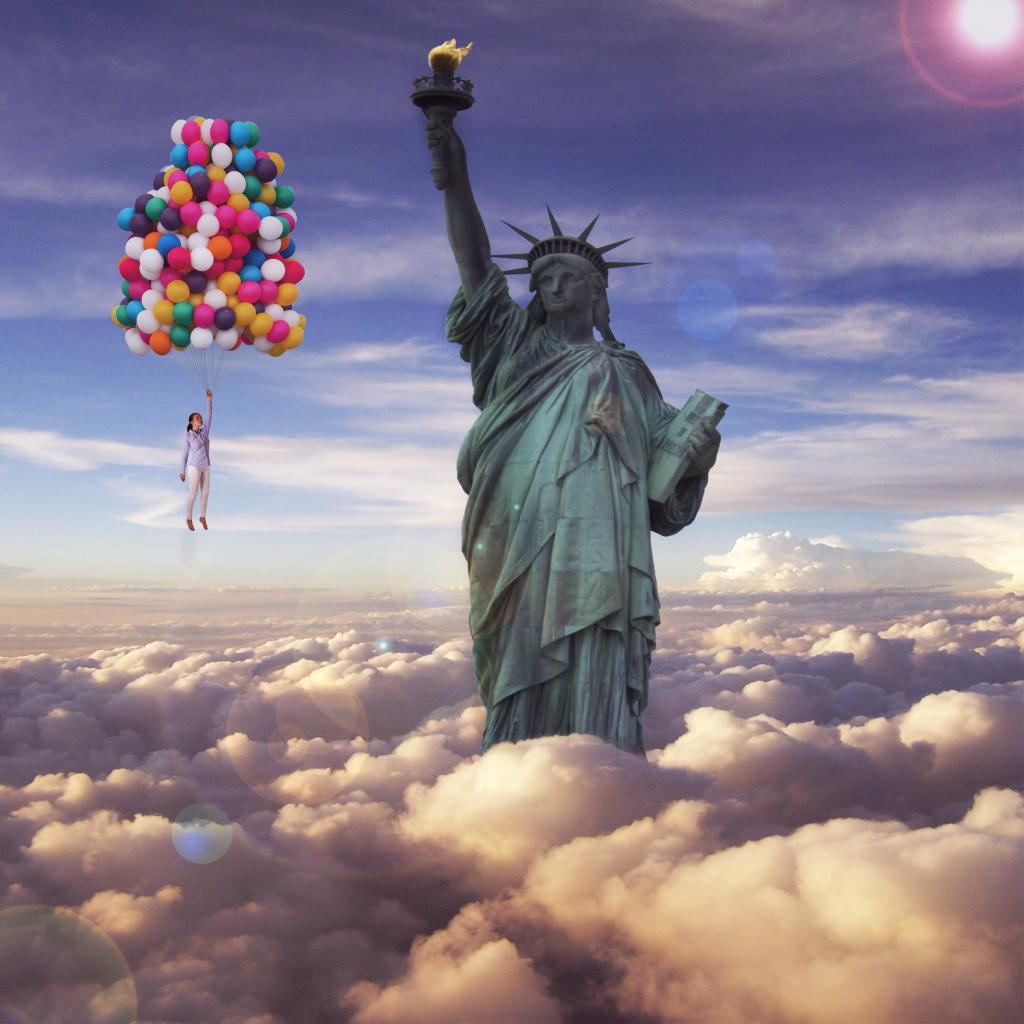 编辑照片的女人拿着束氦气球漂浮在自由女神像的高清壁纸的云层上面